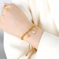 Bracelet en titane plaqué or à perles avec médaillon étoile et pendentif rond nacré sur poignet féminin.