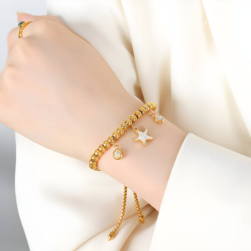 Bracelet en titane plaqué or à perles avec médaillon étoile et pendentif rond nacré sur poignet féminin.