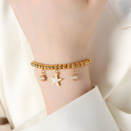 Bracelet en titane plaqué or à billes avec médaillon étoile brillant et deux pampilles rondes sur poignet féminin.