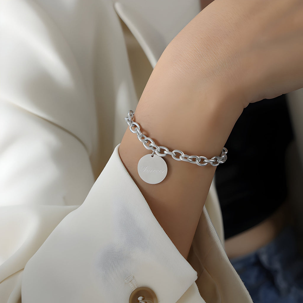 Bracelet chaîne argentée à gros maillons avec médaillon rond lisse sur poignet féminin.