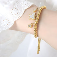 Bracelet en titane plaqué or avec perles rondes et médaillon papillon orné de strass.