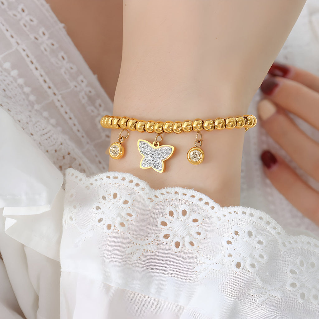 Bracelet en perles dorées avec trois médaillons dont un papillon, style délicat féminin.