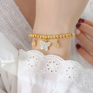 Bracelet en perles dorées avec trois médaillons dont un papillon, style délicat féminin.