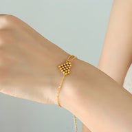 Bracelet en titane plaqué or avec un motif cœur perlé suspendu sur une chaîne fine dorée.