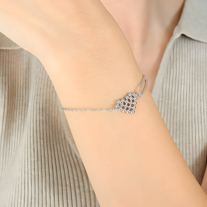 Bracelet fin en titane plaqué argent avec pendentif cœur perlé délicat sur poignet féminin.