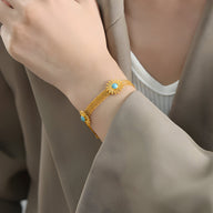 Bracelet doré en titane à motif de fleurs avec pierres turquoise porté au poignet.