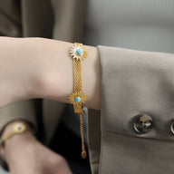 Bracelet en titane plaqué or avec mailles fines et motif fleurs serties de pierres turquoises éclatantes.