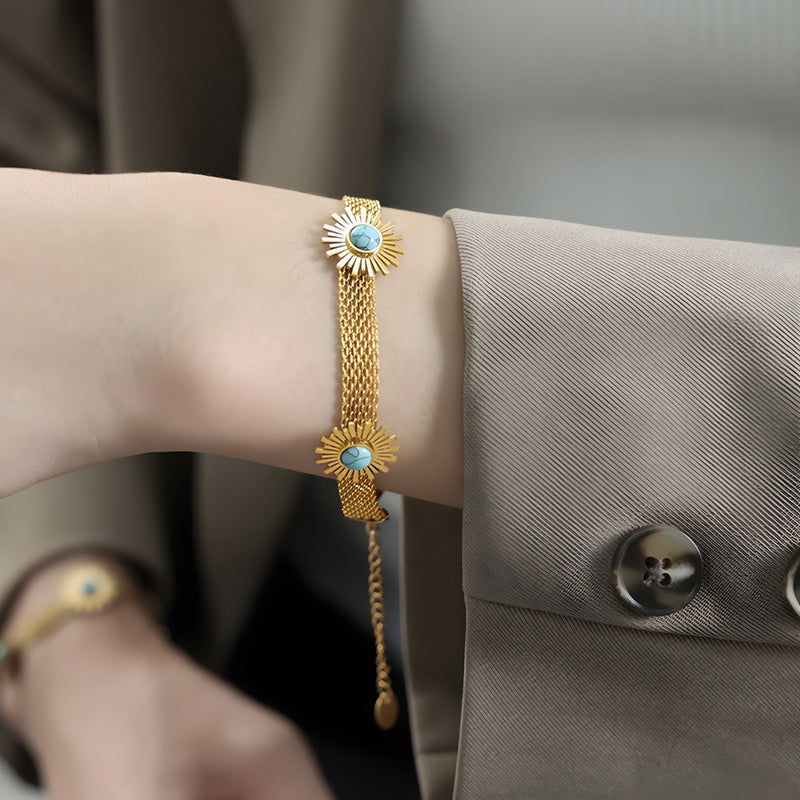 Bracelet en titane plaqué or avec mailles fines et motif fleurs serties de pierres turquoises éclatantes.