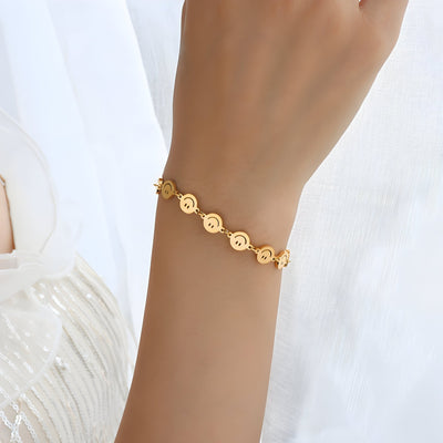 Bracelet en titane plaqué or avec motifs smileys ronds, chaîne fine élégante sur poignet féminin.