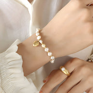 Bracelet en perles blanches avec petit cœur doré en titane plaqué or sur poignet féminin.