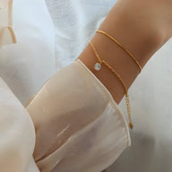 Bracelet fin doré en titane avec chaîne fine et pierre de zircon transparent sur poignet féminin.