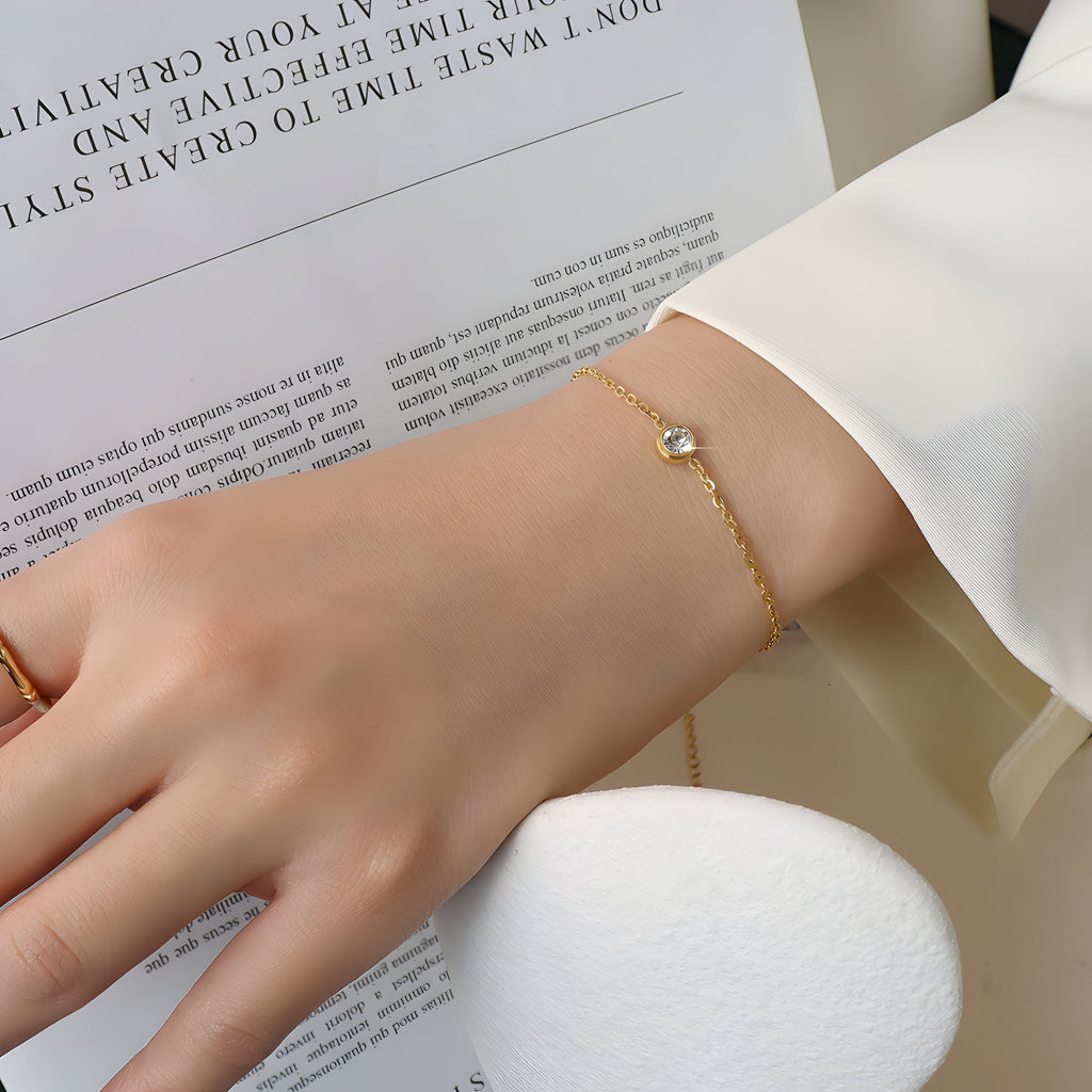 Bracelet fin en titane plaqué or avec diamant rond et chaîne délicate porté au poignet féminin.