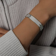 Bracelet gourmette en titane plaqué or, style montre avec plaque personnalisable, porté au poignet, finition brillante.