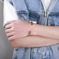 Bracelet jonc argenté en acier inoxydable avec double têtes de loup stylisées porté au poignet.