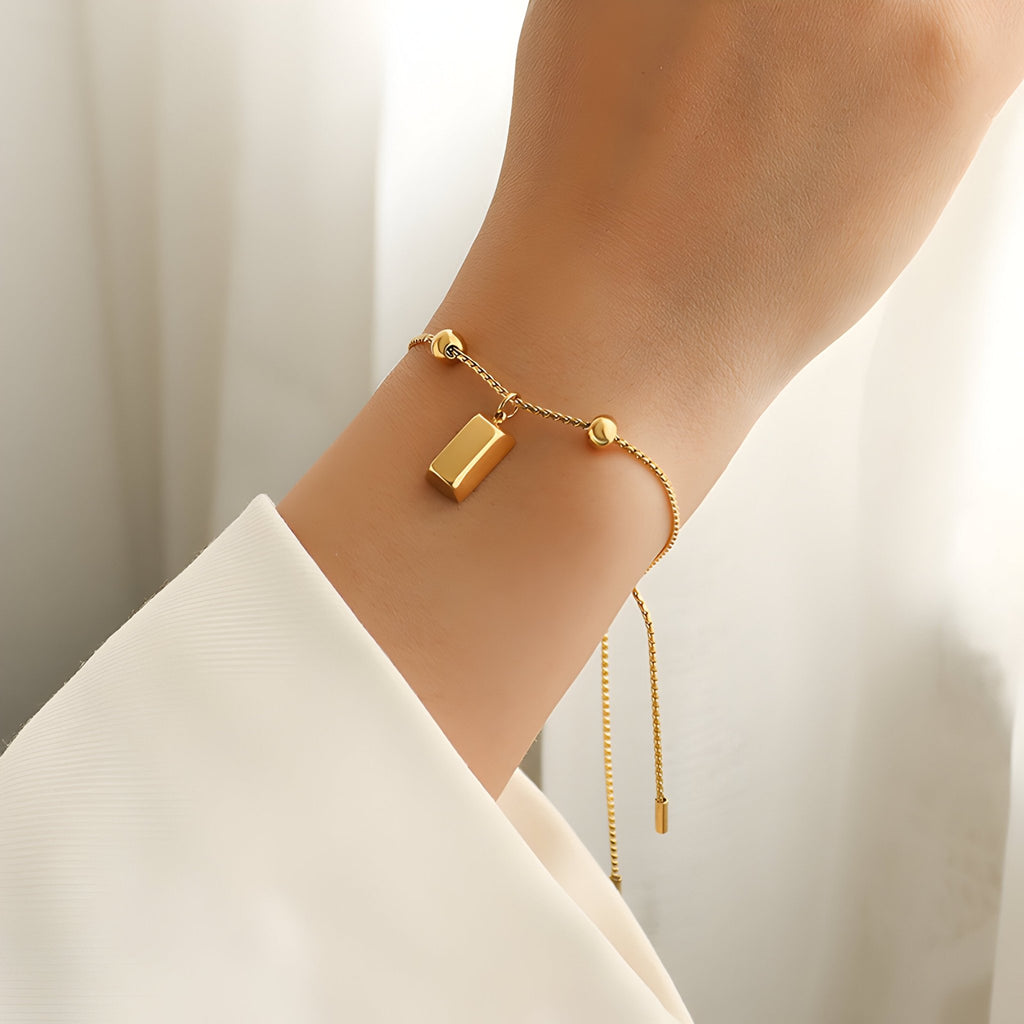 Bracelet jonc en titane plaqué or 18 carats avec pendentif carré et billes rondes, style minimaliste.