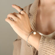 Bracelet jonc en titane plaqué or avec perle blanche ronde, style élégant et minimaliste.