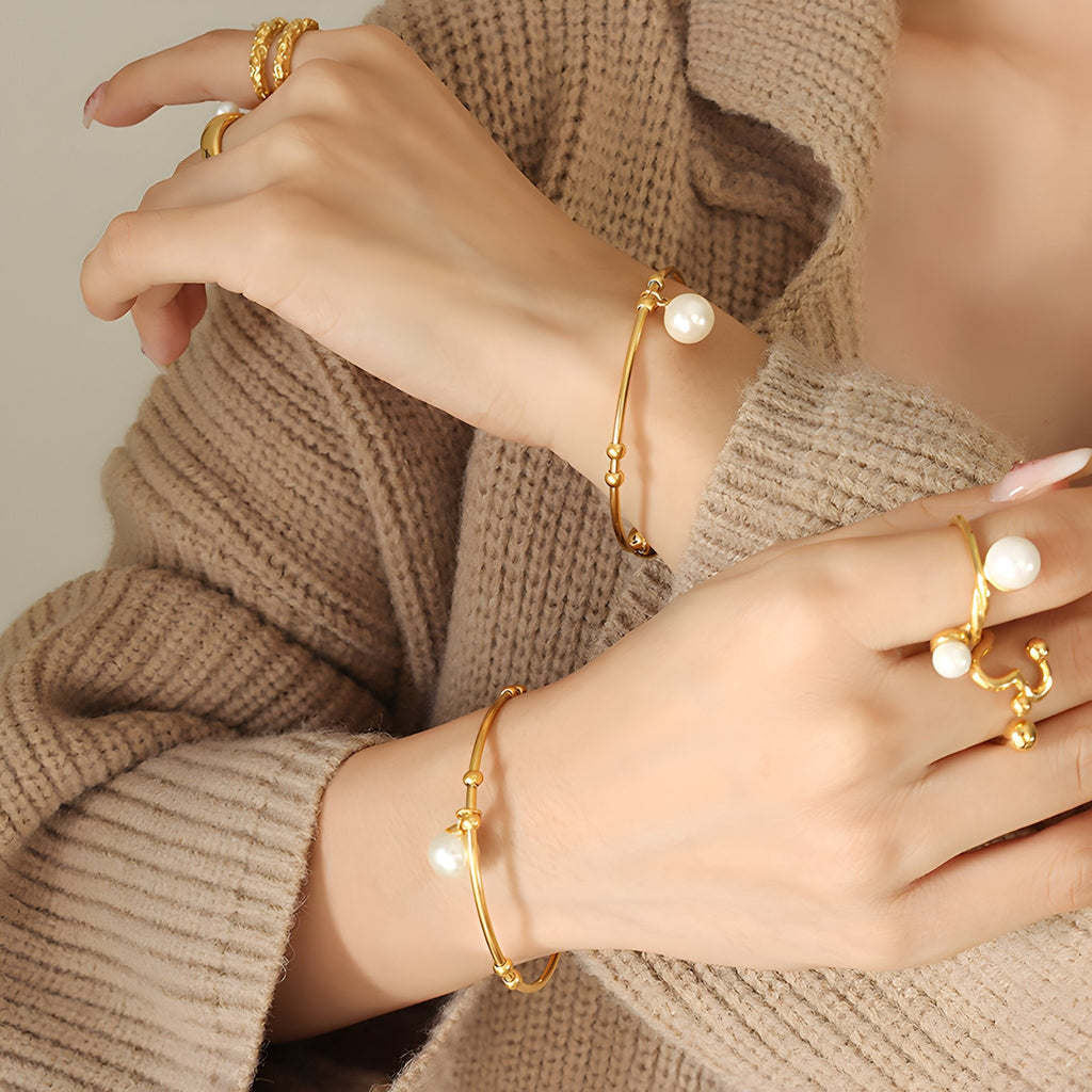 Bracelet jonc en titane plaqué or avec perle blanche élégante portée au poignet.