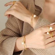 Bracelet jonc en titane plaqué or avec perle blanche élégante portée au poignet.