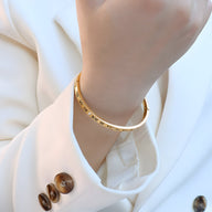 Bracelet jonc en titane plaqué or avec gravures chiffres romains et pierres de zircon sur poignet féminin.