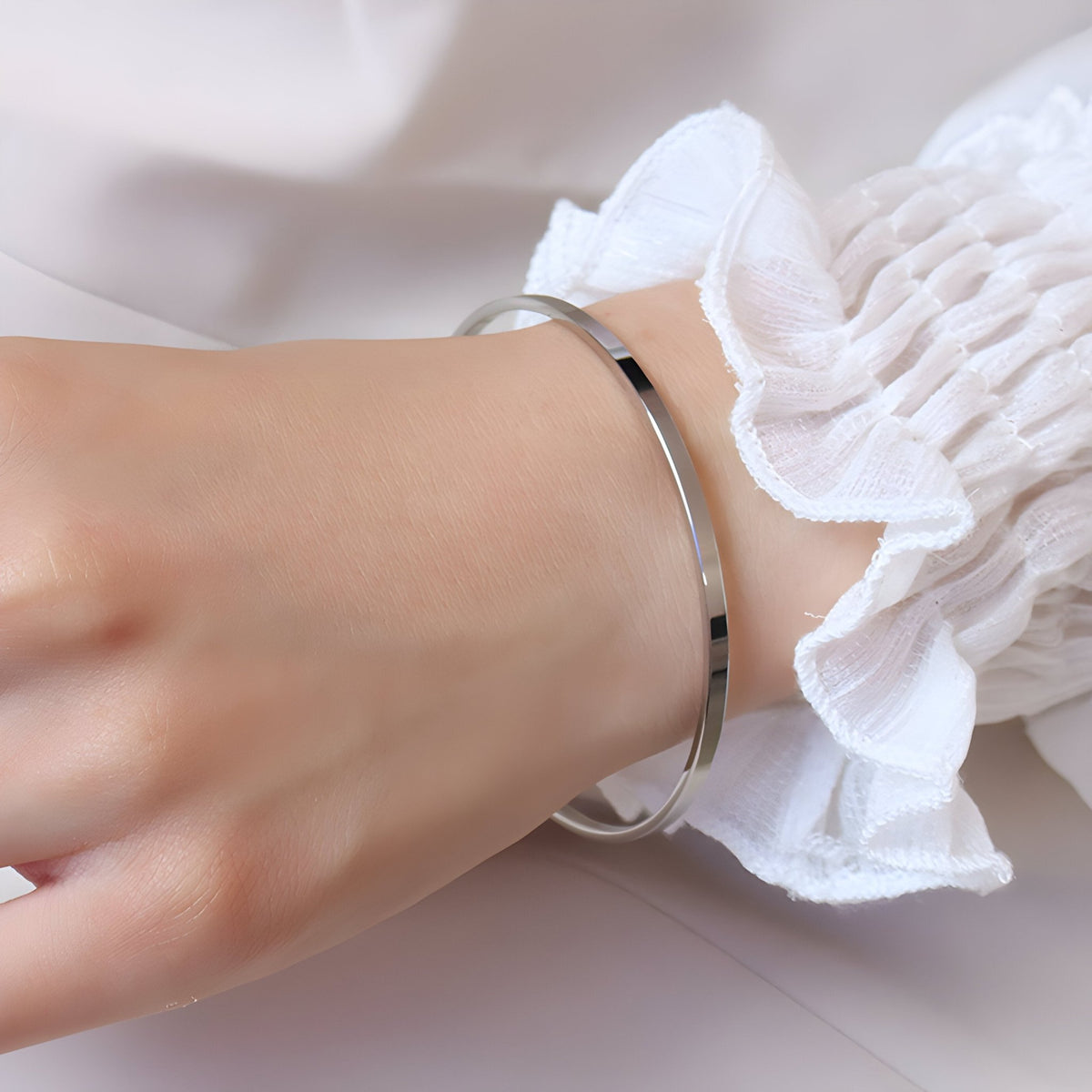 Bracelet jonc fin en titane plaqué or jaune 18 carats porté sur poignet avec manchette blanche à volants.