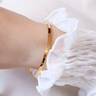 Bracelet jonc fin en titane plaqué or 18 carats lisse et brillant porté au poignet féminin.