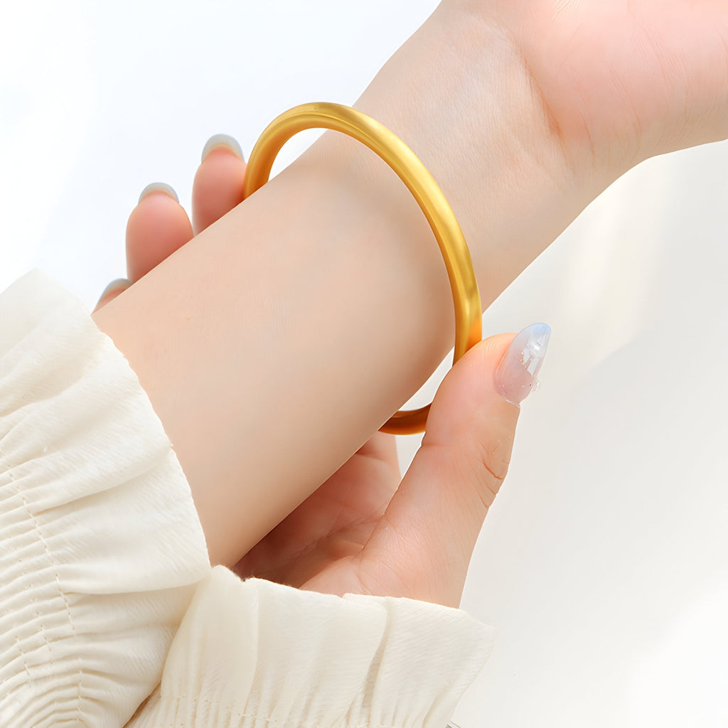 Bracelet jonc fin en titane plaqué or brillant porté au poignet, style épuré et élégant.