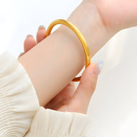 Bracelet jonc fin en titane plaqué or brillant porté au poignet, style épuré et élégant.