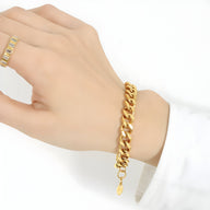 Bracelet maille cubaine épaisse en titane plaqué or brillant, porté au poignet féminin avec breloque ovale.