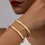 Bracelet manchette double rang en métal doré lisse, design épuré et moderne.