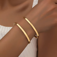 Bracelet manchette double rang fin en métal doré lisse au poignet.