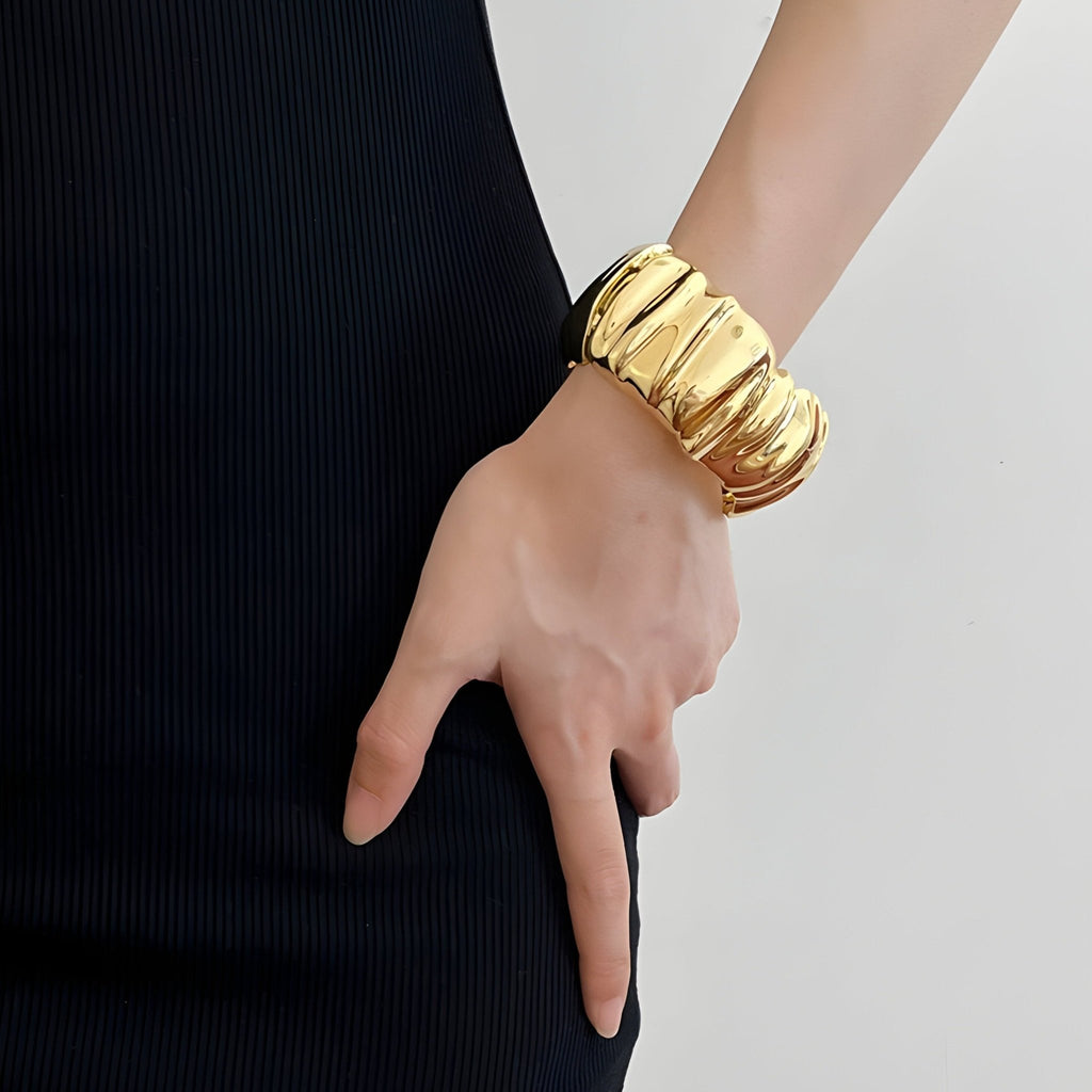 Bracelet manchette or à texture ondulée large porté sur poignet féminin avec robe noire.