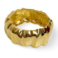 Bracelet manchette en métal doré à texture ondulée, design brillant et sculpté.