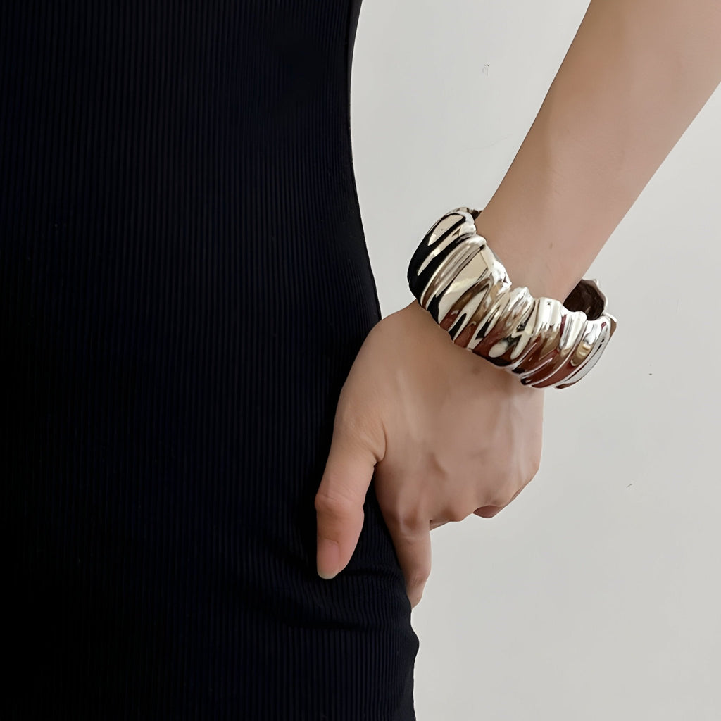 Bracelet manchette or à texture ondulée et finition brillante porté au poignet féminin.