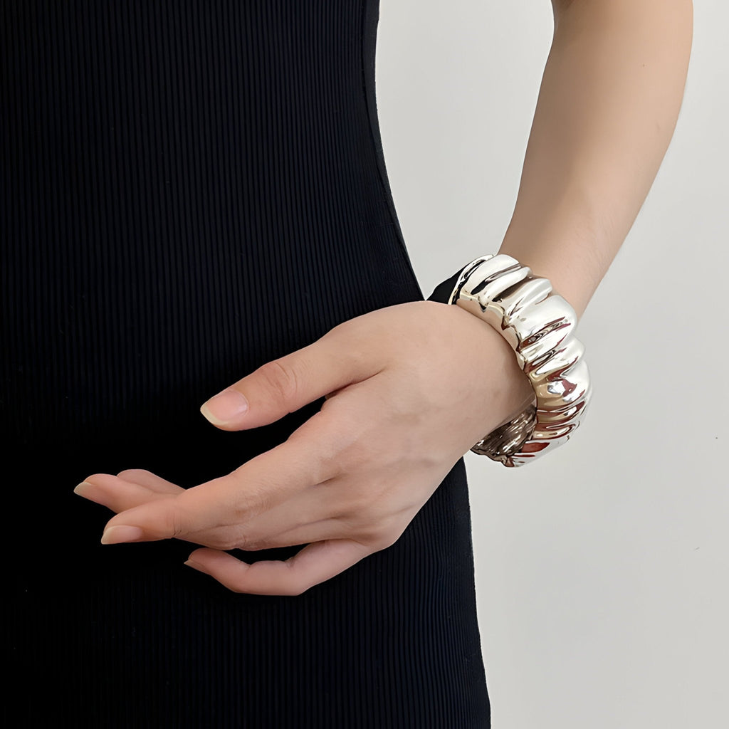 Bracelet manchette ondulé argenté brillant porté sur poignet féminin avec robe noire sans manches.