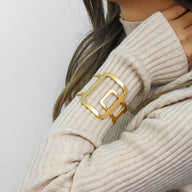 Bracelet manchette doré au design géométrique avec maillons carrés sur pull beige côtelé.