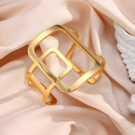 Bracelet manchette en métal doré avec design géométrique ouvert à rectangles entrelacés.