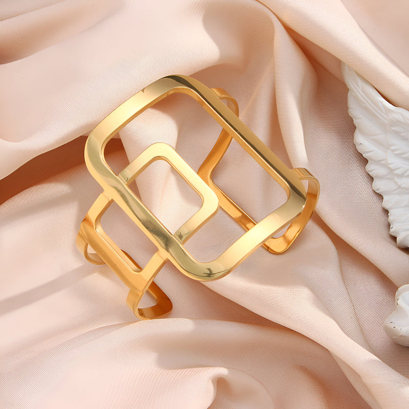 Bracelet manchette en métal doré avec design géométrique ouvert à rectangles entrelacés.