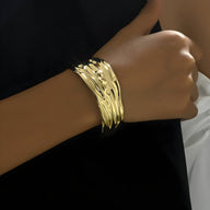 Bracelet manchette doré au design texturé en plusieurs bandes fines entrelacées.