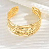 Bracelet manchette doré au design texturé et ondulé, ouverture ajustable.