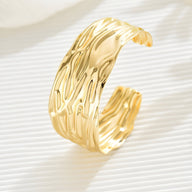 Bracelet manchette en métal doré avec surface texturée ondulée et finition brillante.