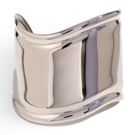 Bracelet manchette large en acier inoxydable argenté avec courbes fluides et finition polie brillante.
