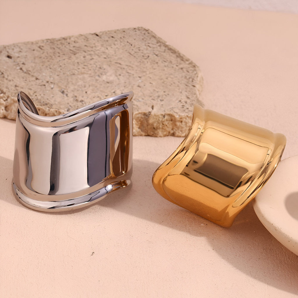 Bracelet manchette large en acier inoxydable poli, versions or et argent, design épuré et incurvé.