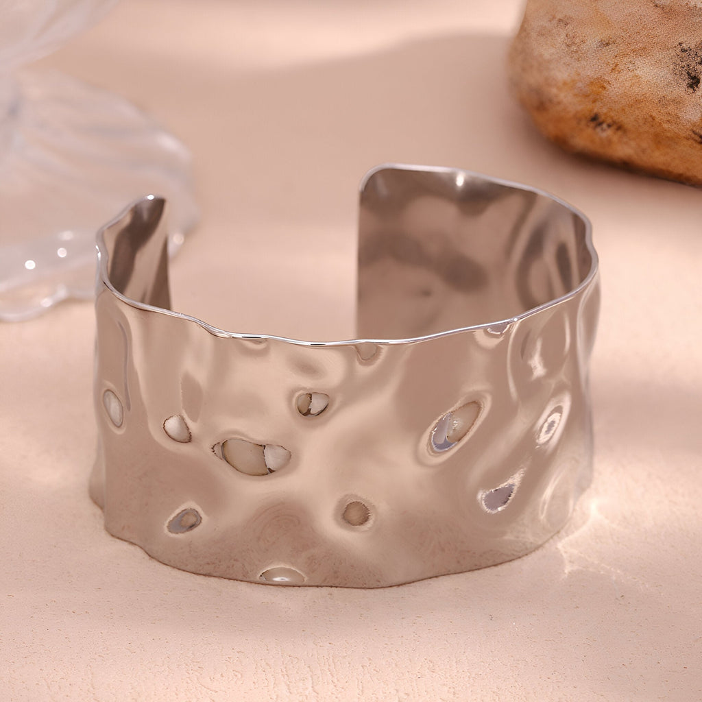 Bracelet manchette en acier inoxydable argenté avec surface ondulée et texture martelée.