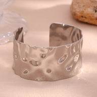 Bracelet manchette en acier inoxydable argenté avec surface ondulée et texture martelée.