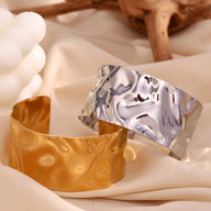 Bracelet manchette ondulé en acier inoxydable, finition or brillant et argenté texturé.