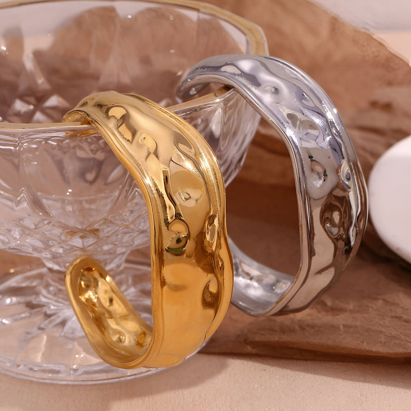 Bracelet manchette sculptural en acier inoxydable, finition dorée brillante et argentée texturée.