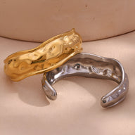 Bracelet manchette sculptural en acier inoxydable doré avec texture irrégulière et modelé argenté lisse et brillant.