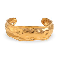 Bracelet manchette sculptural en acier inoxydable doré avec surface ondulée brillante.