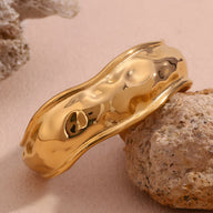 Bracelet manchette doré en acier inoxydable avec surface ondulée et forme sculpturale fluide.