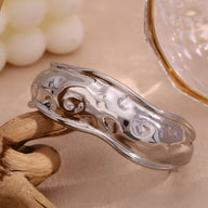 Bracelet manchette sculptural en acier inoxydable argenté à surface ondulée et brillante.